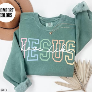 May include: A light green sweatshirt with the words "Love like Jesus" in rainbow colours. The sweatshirt is made of a soft, comfortable material.