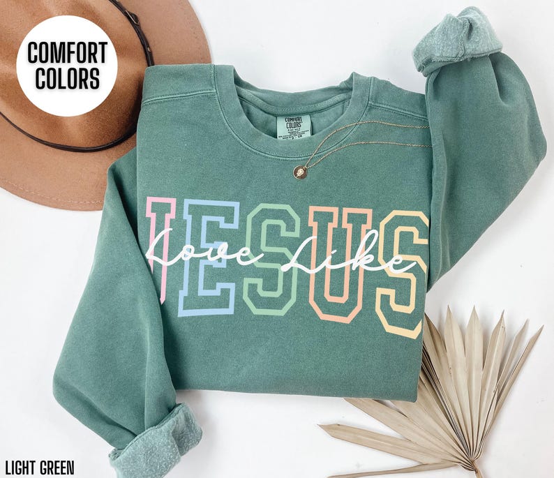 May include: A light green sweatshirt with the words "Love like Jesus" in rainbow colours. The sweatshirt is made of a soft, comfortable material.