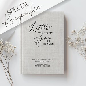 Pu&ograve; includere: Un libro ricordo grigio chiaro intitolato "Lettere a mio figlio in cielo". La copertina presenta una scrittura elegante e il testo "Tutte le cose che vorrei dirti". Il libro include un nome e delle date.