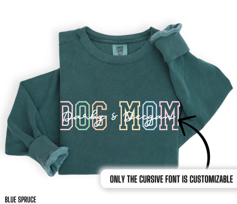 May include: A teal blue sweatshirt with the text "DOG MOM" in colorful block letters. The word "Dog" is in pink, yellow, and green. The word "Mom" is in blue, light blue, and pink. The text "Darby & Regan" is written in cursive in white. The text "ONLY THE CURSIVE FONT IS CUSTOMIZABLE" is written in white at the bottom of the image.