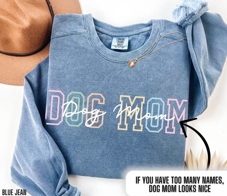 May include: A blue jean sweatshirt with the text "DOG MOM" in rainbow colors. The text "IF YOU HAVE TOO MANY NAMES, DOG MOM LOOKS NICE" is printed below the main text.