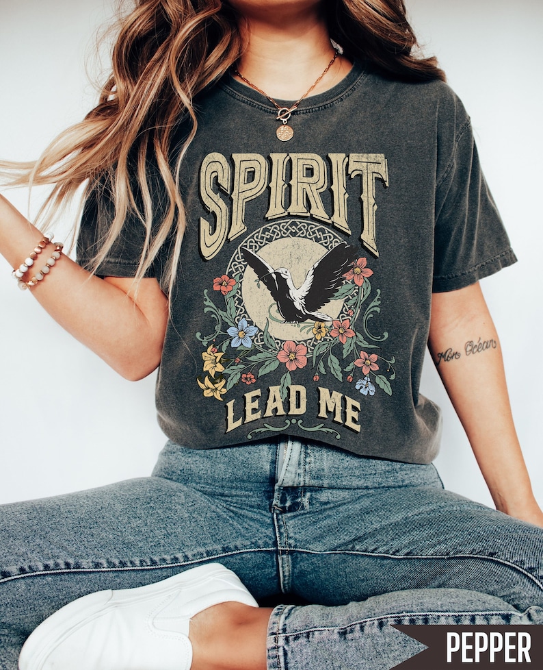 K&ouml;nnte beinhalten: Ein anthrazitfarbenes T-Shirt mit einem Vintage-Grafikdesign, das einen fliegenden Vogel zeigt, der von Blumen umgeben ist, und den Text "SPIRIT LEAD ME".
