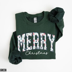 May include: Forest green sweatshirt with a white print that says "Merry Christmas" with a pattern of Christmas trees inside the letters.