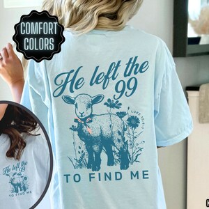 May include: Pale blue t-shirt with a teal illustration of a lamb, flowers, and the text "He left the 99 to find me." The shirt is made of chambray fabric and features the words "Comfort Colors."