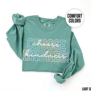May include: Light green long-sleeve t-shirt with the text "Choose Kindness" in rainbow colors. The shirt is made of a soft, comfortable material.