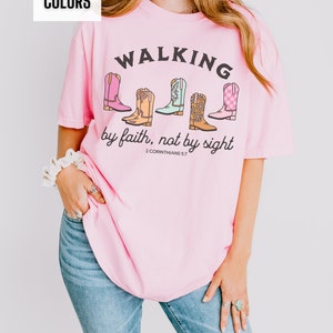 Puede incluir: Camiseta rosa con un gr&aacute;fico de botas de vaquero y el texto "WALKING by faith, not by sight 2 CORINTHIANS 5:7"