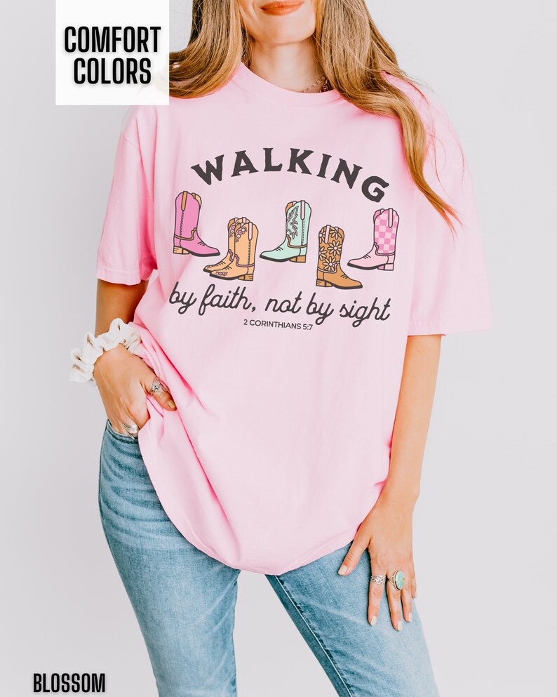 Puede incluir: Camiseta rosa con un gr&aacute;fico de botas de vaquero y el texto "WALKING by faith, not by sight 2 CORINTHIANS 5:7"