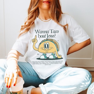May include: White t-shirt with a cartoon taco graphic and the text "Wanna Taco bout Jesus?"  The taco is wearing sneakers and has a happy expression.  The text "FOR GOD SO LOVED THE WORLD THAT HE GAVE HIS ONE AND ONLY SON, THAT WHOEVER BELIEVES IN HIM SHALL NOT PERISH BUT HAVE ETERNAL LIFE. JOHN 3:16" is printed below the taco.