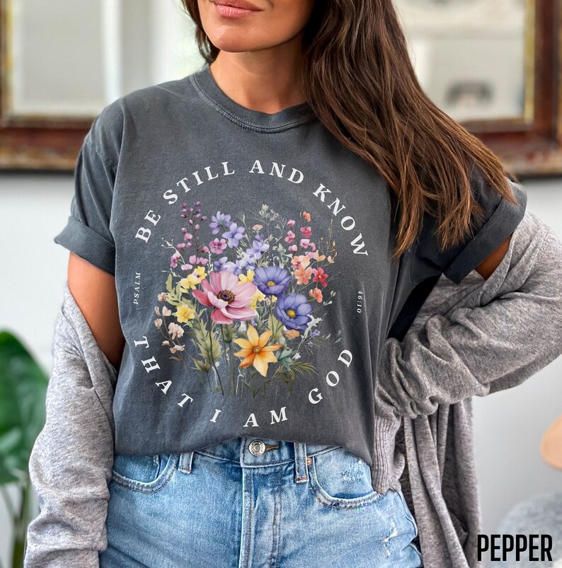 May include: A gray t-shirt with a floral design and the text "Be still and know that I am God" with the scripture reference "Psalm 46:10".