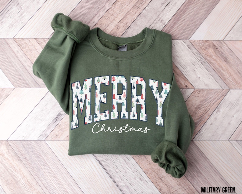 May include: A green sweatshirt with a white "Merry Christmas" graphic featuring a pattern of Christmas trees. The text is in a collegiate font.