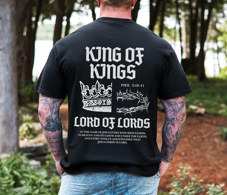 Christian shirt featuring “King of Kings, Lord of Lords” and Philippians 2:10–11 with a powerful front and back design. The artwork shows a half modern crown and half crown of thorns representing Jesus’ sacrifice and kingship. Available in short sleeve, long sleeve, sweatshirt, and youth tee. Perfect faith-based apparel for men, women, and kids who want to share their Christian belief in style.