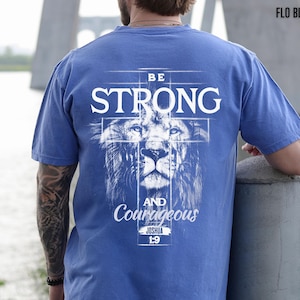 May include: Blue t-shirt with the words "BE STRONG" in white, above a lion's face, and "AND Courageous" below. The text "JOSHUA 1:9" is also printed on the shirt. The shirt is a solid blue color.
