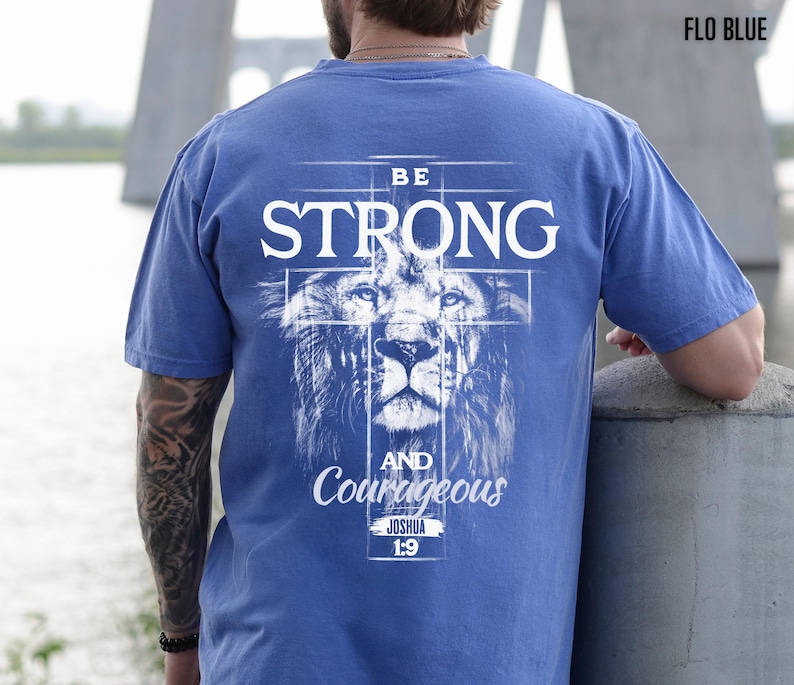 May include: Blue t-shirt with the words "BE STRONG" in white, above a lion's face, and "AND Courageous" below. The text "JOSHUA 1:9" is also printed on the shirt. The shirt is a solid blue color.