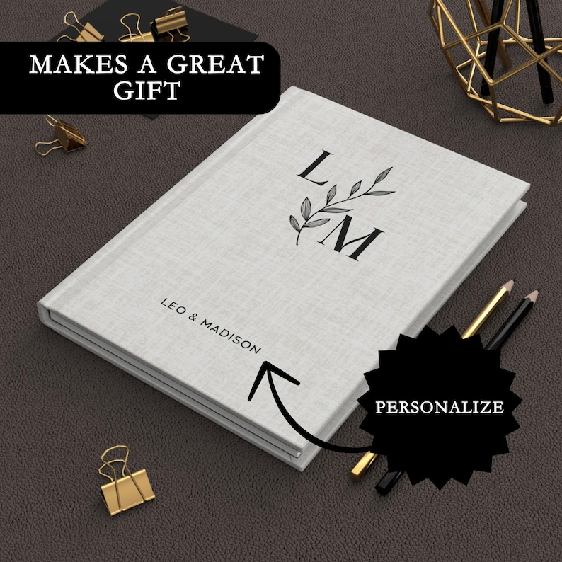 May include: A white linen journal with a personalised monogram of the letters "L" and "M" with a leafy design. The text "Leo & Madison" is printed below the monogram. The journal is a great gift.