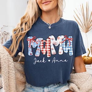 May include: Navy blue t-shirt with the word "MAMA" in a patriotic design, featuring red, white, and blue patterns and bows. The names "Jack" and "Anna" are written below the word "MAMA".