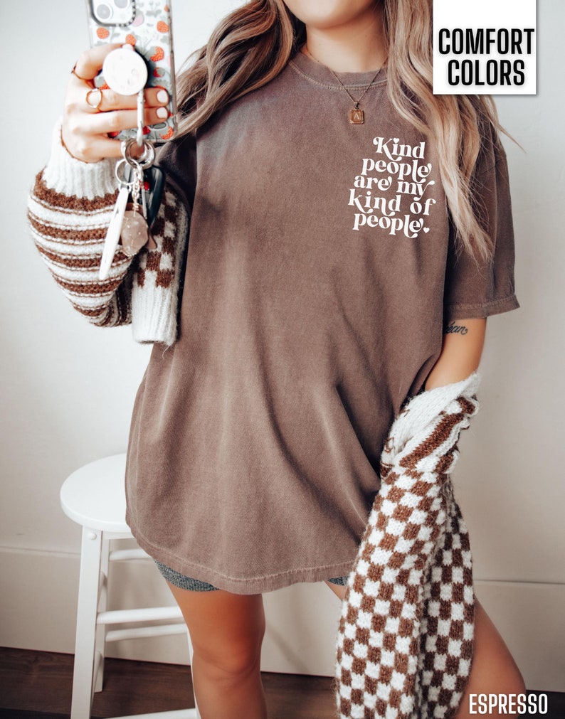 May include: A brown t-shirt with the text "Kind people are my kind of people" in white. The shirt is being worn by a person with a brown and white checkered sweater.
