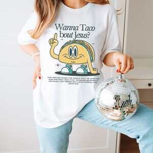 May include: White t-shirt with a cartoon taco wearing sneakers and a speech bubble that says "Wanna Taco bout Jesus?"  The shirt also has a Bible verse from John 3:16.