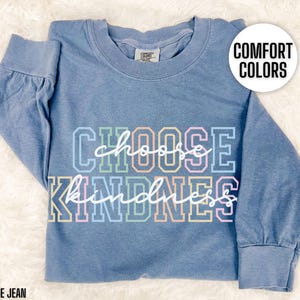 May include: A blue jean long-sleeve t-shirt with the text "Choose Kindness" in rainbow colors. The text is in a bold, blocky font.