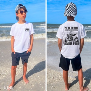May include: A white t-shirt with black text that says "PUT ON THE WHOLE ARMOUR OF GOD" and a black and white illustration of a knight on a horse. The shirt is being worn by a person wearing black shorts and a black and white checkered hat.