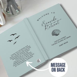 May include: A light blue guest book with the words "Welcome to Seaside Retreat" and a seashell illustration. The address "1316 5th Street Topsail Island, NC 28445" and the words "Guest Book" are printed on the cover. The back cover has a message that reads "Thank you for being our guest. We invite you to share your seaside adventures and memories in these pages, creating a lasting collection of cherished moments for all who visit. Your words add to the magic of this coastal paradise."