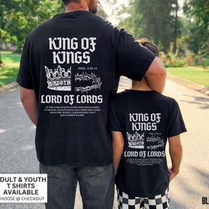 May include: Black t-shirts with white text featuring "King of Kings" and "Lord of Lords" with a crown and a crown of thorns design. The shirts have the text "Phil 2:10-11" and a Bible verse. Adult and youth sizes are available.