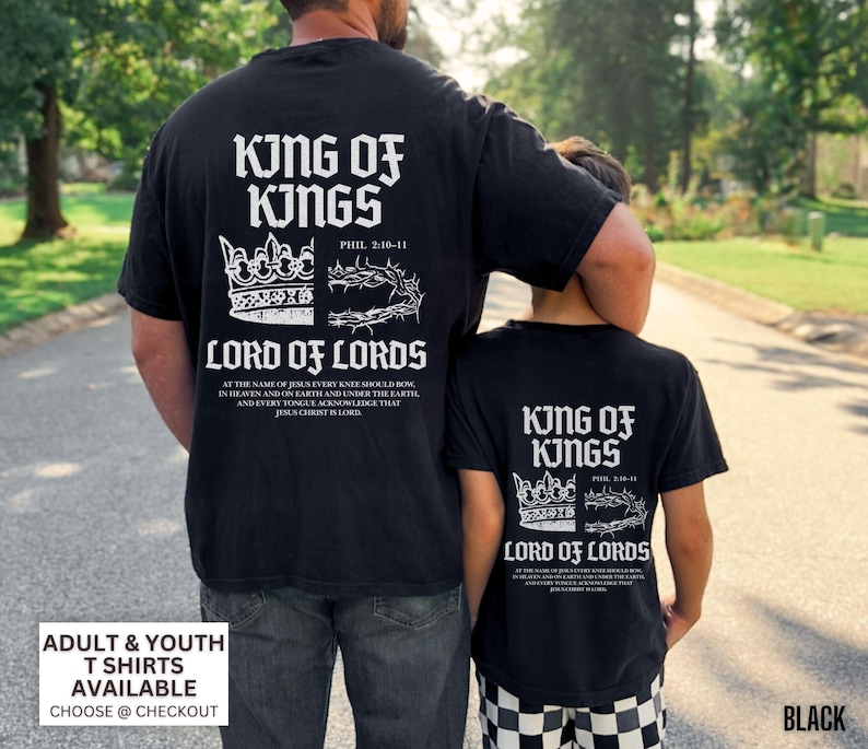 May include: Black t-shirts with white text featuring "King of Kings" and "Lord of Lords" with a crown and a crown of thorns design. The shirts have the text "Phil 2:10-11" and a Bible verse. Adult and youth sizes are available.