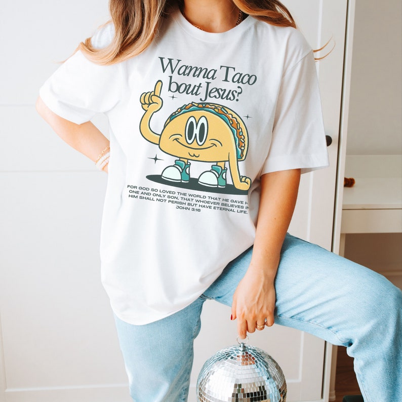 May include: White t-shirt with a cartoon taco graphic and the text "Wanna Taco bout Jesus?"  The taco is wearing sneakers and has a happy face. The shirt also includes a bible verse: "For God so loved the world that he gave his one and only Son, that whoever believes in him shall not perish but have eternal life. John 3:16"