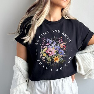 May include: Black cropped t-shirt with a floral design and the text "Be still and know that I am God" with the reference "Psalm 46:10".