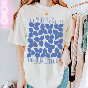 May include: A white t-shirt with a blue floral design and the text "Where the Spirit of the Lord is There is Freedom 2 Corinthians 3:17".