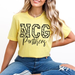 May include: A yellow t-shirt with the text "NCG Panthers" in black. The letters "NCG" have a leopard print design. The word "Panthers" is written in a script font. The word "YELLOW" is at the bottom left.