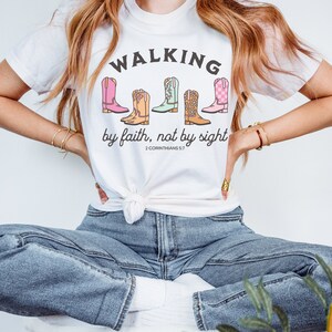 Puede incluir: Camiseta blanca con un gr&aacute;fico de botas de vaquero de colores y el texto "Walking by faith, not by sight 2 Corinthians 5:7".