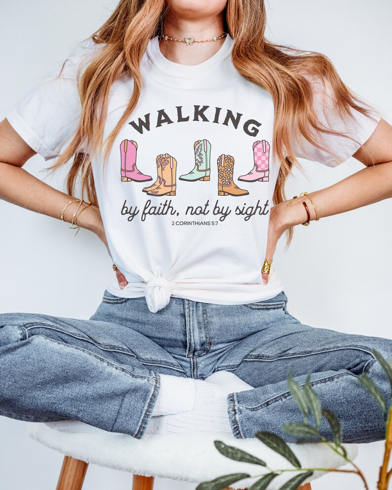 Puede incluir: Camiseta blanca con un gr&aacute;fico de botas de vaquero de colores y el texto "Walking by faith, not by sight 2 Corinthians 5:7".