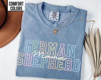 May include: A blue jean t-shirt with the text "German Shepherd Mama" in rainbow colors. The shirt is made of a soft, comfortable material and has a distressed look.