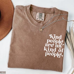 May include: A brown t-shirt with the text "Kind people are my kind of people" in white lettering. The shirt is made of a soft, comfortable material.