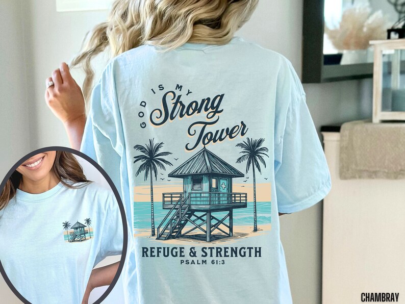 Puede incluir: Camiseta azul claro con un gr&aacute;fico de una escena de playa con una torre de salvavidas y palmeras. El texto "God is my Strong Tower" y "Refuge & Strength Psalm 61:3" est&aacute; impreso en la camiseta.