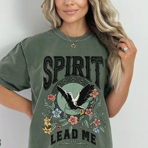 K&ouml;nnte beinhalten: Ein gr&uuml;nes T-Shirt mit einem Vintage-Motiv, das einen Vogel im Flug, Blumen und den Text "SPIRIT LEAD ME" zeigt.
