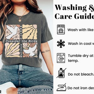 Op de afbeelding: Een grijs T-shirt met een grafisch ontwerp met een duif, bloemen en de tekst "Consider the Birds" en "Matthew 6:26". De afbeelding bevat ook een was- en onderhoudsgids met instructies voor het wassen, drogen en strijken van het shirt.