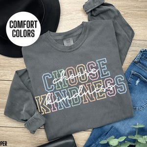 May include: A long-sleeved, dark gray t-shirt with the text "Choose Kindness" in rainbow colors. The shirt is made of a soft, comfortable material.