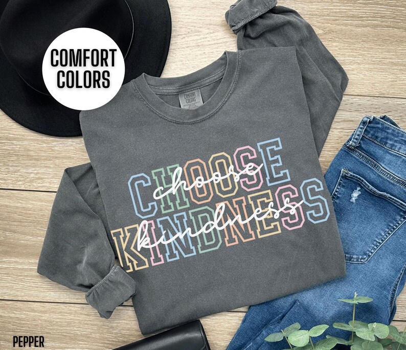 May include: A long-sleeved, dark gray t-shirt with the text "Choose Kindness" in rainbow colors. The shirt is made of a soft, comfortable material.