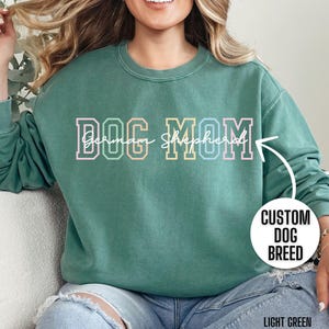 May include: A light green sweatshirt with the text "DOG MOM German Shepherd" in rainbow colors. The sweatshirt is a crew neck and has a relaxed fit.
