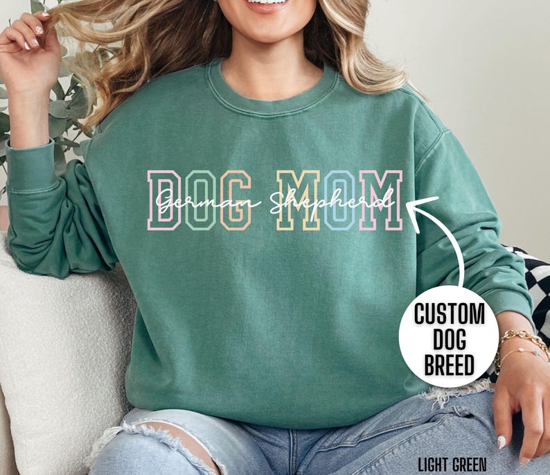May include: A light green sweatshirt with the text "DOG MOM German Shepherd" in rainbow colors. The sweatshirt is a crew neck and has a relaxed fit.