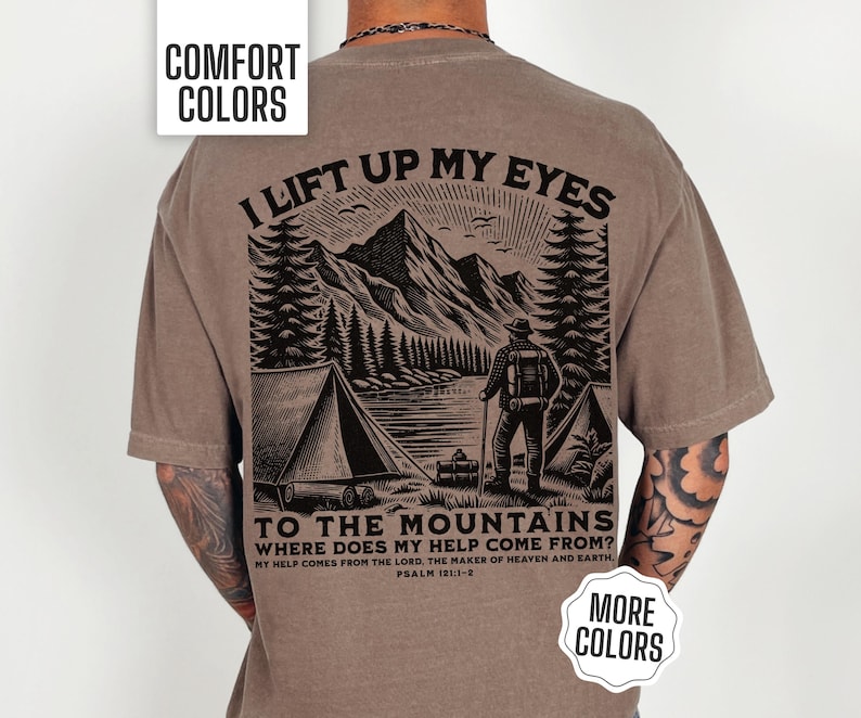Christian men’s Comfort Colors shirt showing a man standing at his camp looking toward the mountains and a lake with the Bible verse “I lift my eyes to the mountains” from Psalm 121:1. Available in short sleeve, long sleeve, sweatshirt, and youth tee sizes so fathers and sons can match. Perfect for Christian campers, hikers, and outdoor enthusiasts who love faith-based apparel and scenic nature designs.