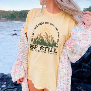 May include: A yellow t-shirt with a mountain scene and the text "The Lord will fight for you; you need only to be still. Exodus 14:14"