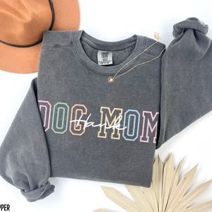 May include: Gray sweatshirt with a colorful "Dog Mom" graphic. The sweatshirt has a distressed look and a crew neck.
