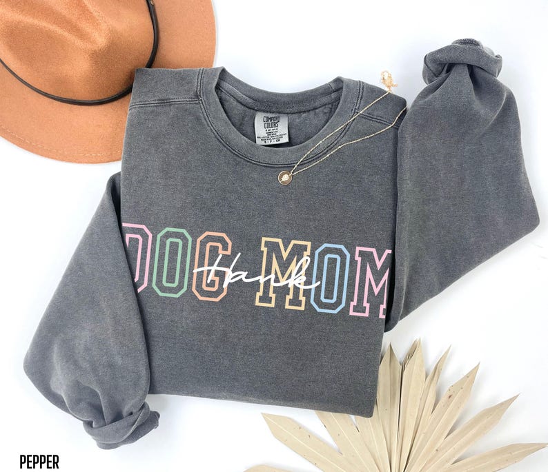 May include: Gray sweatshirt with a colorful "Dog Mom" graphic. The sweatshirt has a distressed look and a crew neck.
