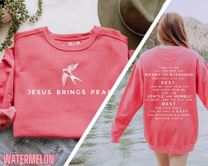May include: A pink sweatshirt with a white bird graphic and the text "JESUS BRINGS PEACE" on the front. The back of the sweatshirt has the text "COME TO ME, ALL YOU WHO ARE WEARY AND BURDENED, AND I WILL GIVE YOU REST. TAKE MY YOKE UPON YOU AND LEARN FROM ME. FOR I AM GENTLE AND HUMBLE IN HEART, AND YOU WILL FIND REST FOR YOUR SOULS. FOR MY YOKE IS EASY AND MY BURDEN IS LIGHT. MATTHEW 11:26-30"