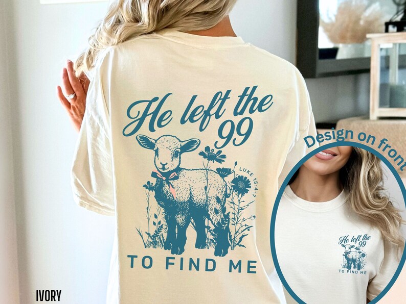 May include: Cream-coloured t-shirt with a teal graphic on the back. The design includes a lamb, flowers, and the text "He left the 99 to find me." The front design is also visible. A relaxed fit, casual style.