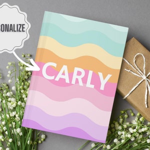 May include: A personalized notebook with a colorful wavy design in shades of pink, orange, yellow, blue, and purple. The name "Carly" is printed in white on the front cover.