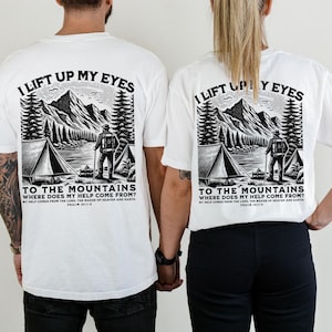May include: White t-shirts with a black and white graphic of a mountain scene, a tent, and a person with a backpack. The text on the shirt reads "I lift up my eyes to the mountains, where does my help come from?" Psalm 121:1-2.