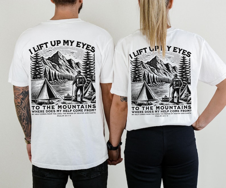 May include: White t-shirts with a black and white graphic of a mountain scene, a tent, and a person with a backpack. The text on the shirt reads "I lift up my eyes to the mountains, where does my help come from?" Psalm 121:1-2.